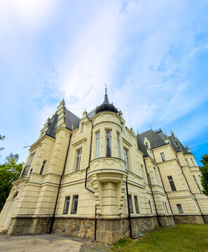 Architectural corner view of Budmerice Manor with turret and windows. Low angle shot of yellow palace wall with rounded balcony tower and stone foundation.