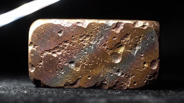 Close up of textured bronze copper ingot with porous surface under sweeping directional light