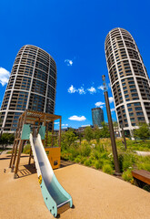 Children playground slide with modern towers in background. Wooden play structure stands in a landscaped park below tall modern buildings on a sunny day. © Анна Терелюк