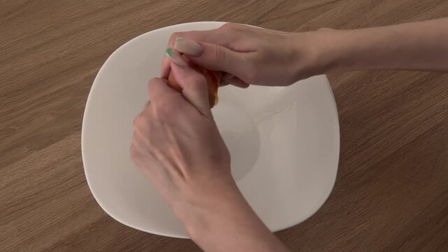 Feminine hands cracking a fresh brown egg into a white bowl on a wooden table, preparing breakfast