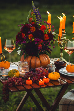Garden romantic party outside with wine, cheese, fruits. Field or meadow, family event, cozy autumn atmosphere, fall vibes. Wooden furniture, pumpkin with flowers as centrepiece, fresh red dahlia