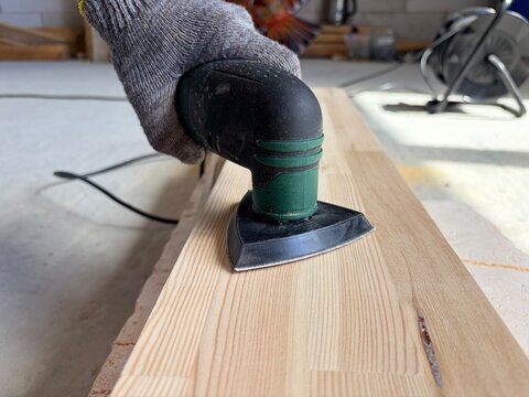 a worker's hand wearing a grey knitted protective glove operating an electric detail sander. Renovation or construction work