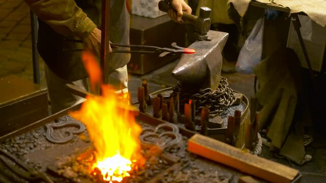 Blacksmith forging glowing metal on an anvil. Professional blacksmith using tongs and a hammer to shape a piece of incandescent steel on an anvil, with the bright flames of the forge