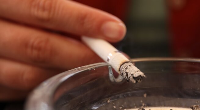 Woman flicking ash from cigarette into ashtray outdoors, closeup