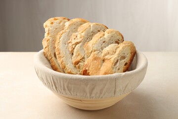 Obraz premium Fresh bread slices in basket on beige table, closeup