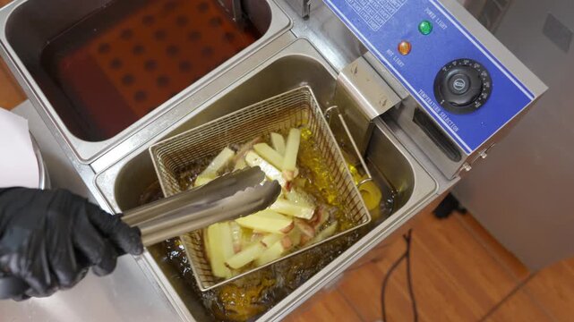 Chef deep frying fresh cut french fries in commercial kitchen