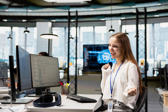 Happy female engineer dances on an office chair after streamlining workflows with AI, celebrating the successful implementation of neural networks and progress on a technology project.