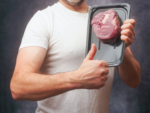 Masculine male butcher in white shirt showing top quality T-bone steak in vacuum package for extra freshness of the product. Top price beef promotion. Meat industry high value cut.
