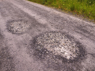 Gravel road with potholes. Foggy weather. Green bushes and grass along roadside. Rural country side area. Surface damaged due to hard weather conditions and poorly done job. © mark_gusev