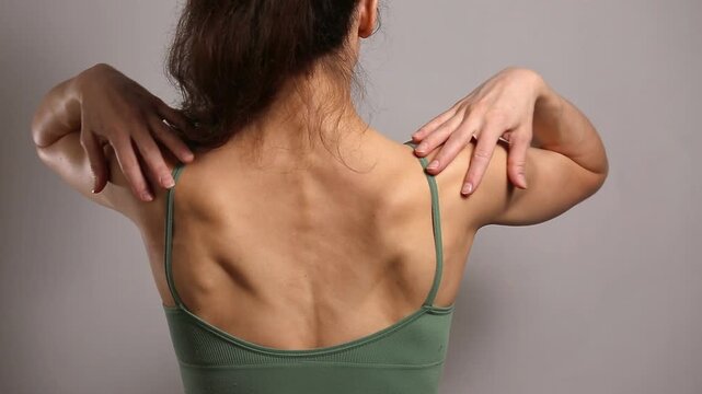 Fit woman performing shoulder and upper back exercises in sportswear, demonstrating mobility, posture, muscle training and wellness in a clean studio setting.