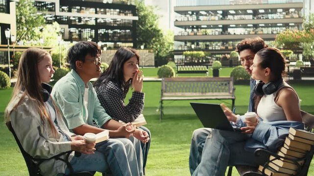 Students discuss coursework on a campus bench with diverse classmates using a laptop and study materials for collaborative project work and peer learning.