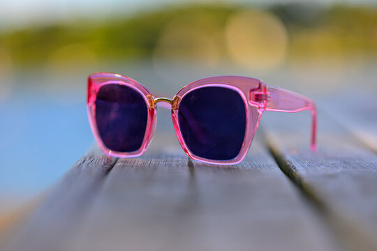 Pink translucent sunglasses resting on wooden bench outdoors.