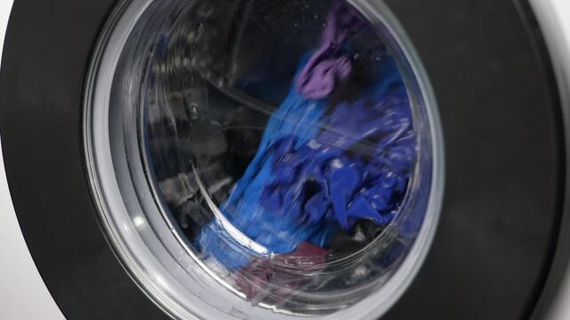 Washing machine drum spinning with clothes. Close-up view of a washing machine drum spinning with colorful clothes during a laundry cycle, showcasing the spinning, tumbling, and cleaning process