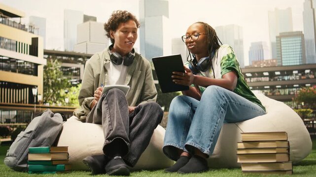 Classmates share ideas around an open laptop while seated on campus beanbags, during peer tutoring, within collaborative group study.