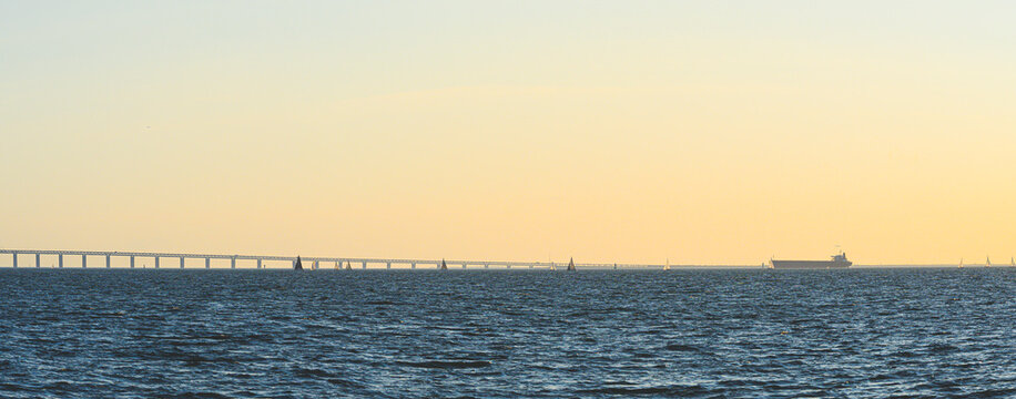 Cargo ship and sailboats crossing Oresund during hazy evening.
