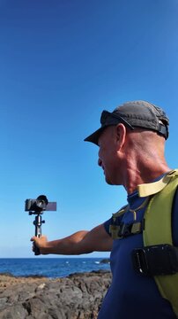 Middle-aged man recording a vlog for his podcast outdoors on a sunny day in Lanzarote, creating content about lifestyle and mental health for his social media channels using a camera on a gimbal