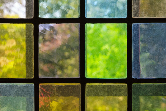 Close-up view of a grid of medieval multi-colored stained glass windows with textured surfaces filtering natural light and greenery.