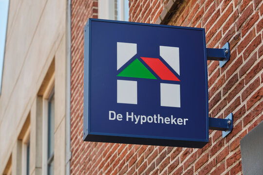 A blue sign with the De Hypotheker logo and name is mounted on a textured brick wall. De Hypotheker is a Dutch mortgage intermediary.