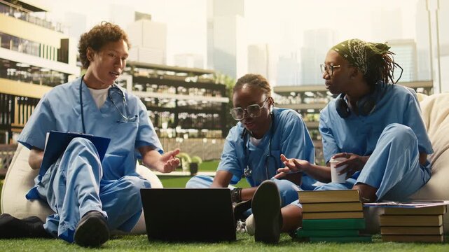 The diverse group of medical students collaborates with a laptop on campus, combining discussion with peer tutoring and group study outdoors.