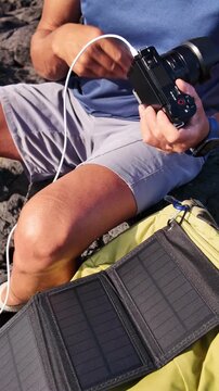 Middle-aged content creator sitting on volcanic rocks, charging his mirrorless camera with a portable solar panel, embodying a nomadic lifestyle and embracing renewable energy for his equipment