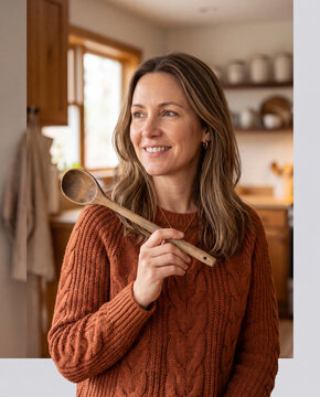 Smiling woman in rust knit sweater holding a wooden ladle in kitchen