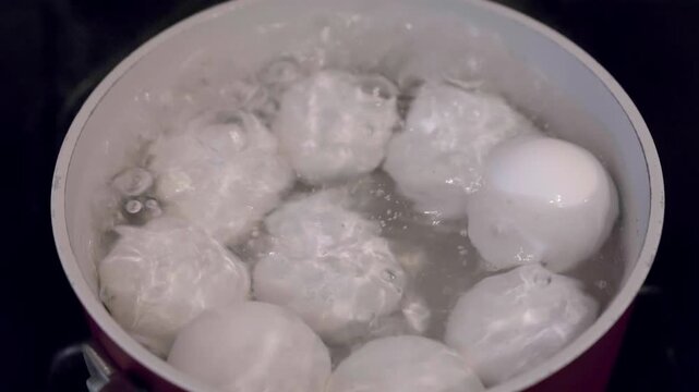 White chicken eggs boiling in a pot of hot bubbling water on a stove top