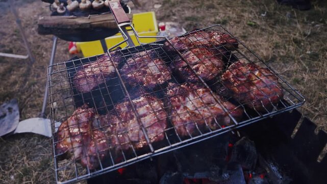 Grilled meat sizzling on a barbecue rack with smoke rising, surrounded by grass and outdoor cooking equipment in a vibrant summer setting