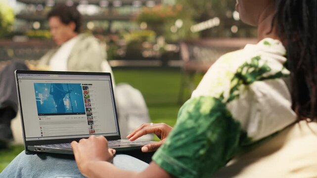The African American student listens to an online concert video during a campus study break, with a broadcast music performance playing on the laptop.