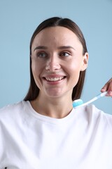 Naklejka na ściany i meble Woman holding toothbrush with toothpaste on light blue background