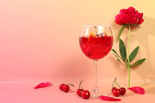 Cherry Aperol Spritz on the rocks for a party. Modern still life with a summer alcoholic cocktail and peony flowers against a sunny background. Minimalistic concept for a bar or cafe.