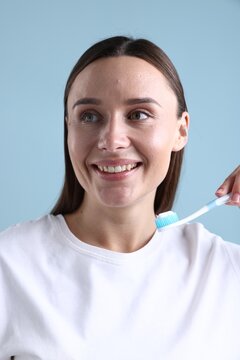 Woman holding toothbrush with toothpaste on light blue background