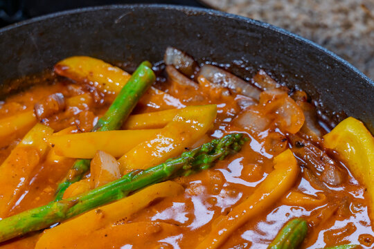 Delicious vegetable curry simmering inside skillet with asparagus spears