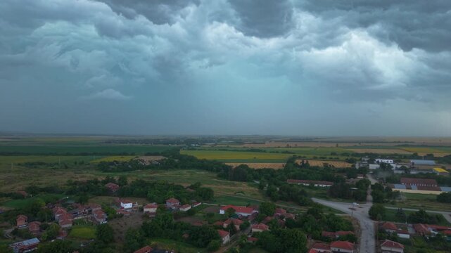 Dramatic supercell thunderstorm forming over rural farmland, with massive dark shelf clouds, heavy rainfall and turbulent storm structure creating an ominous severe weather landscape.