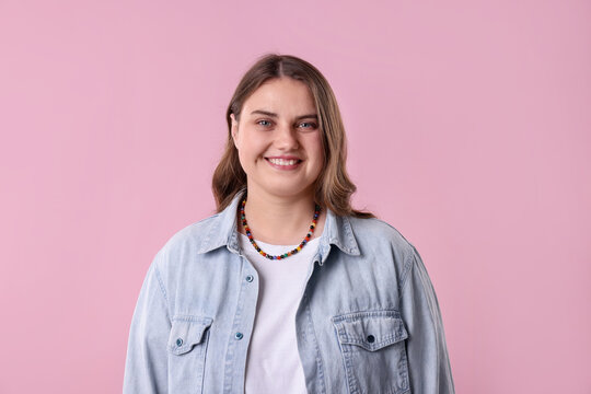 Portrait of plus size model in denim shirt on pink background. Beautiful young overweight woman