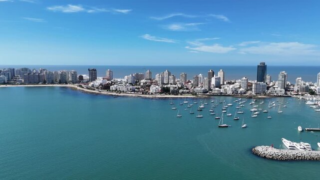 Cinematic drone footage of Punta del Este Marina featuring luxury yachts, sailboats and the city skyline on a sunny day in Uruguay.