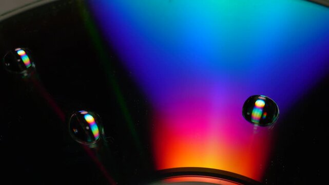 Macro video of moving light illuminating water droplets on a quadrant of an iridescent CD-ROM disk
