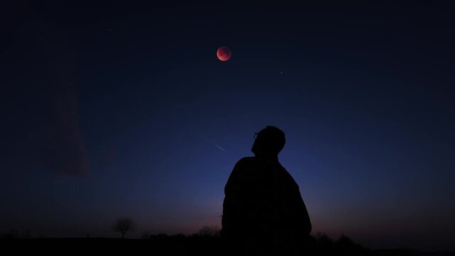 Silhouette of a person in nature observing night sky, Moon, stars and planets from a remote location.