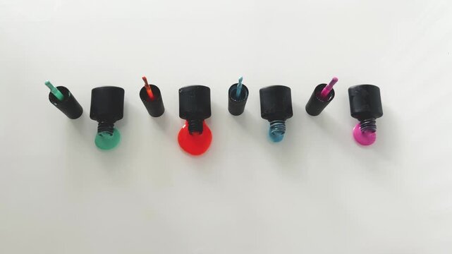 Open black bottles of colorful nail polish spilling onto a clean white surface