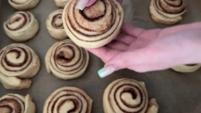 Female hands placing a raw cinnamon roll on a baking sheet before putting it in the oven