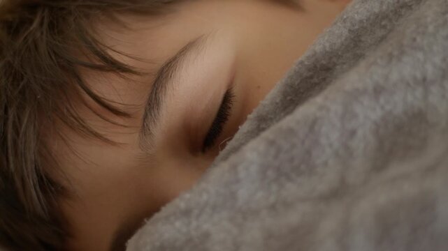 Child sleeps, eyes half-open, smiling softly under blanket. Warm, peaceful moment. Calm, gentle expression. Ideal for quiet, bedtime, or family scenes