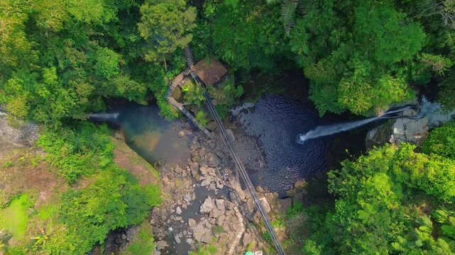 Aerial view of Curug Telu waterfall surrounded by lush tropical forest and rocky terrain in Baturaden, Jawa Tengah, Indonesia.