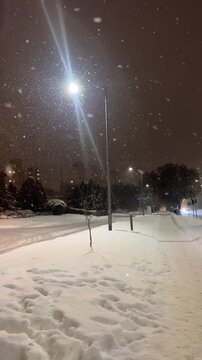 Snowflakes falling on a deserted city sidewalk under the glow of a street lamp on a winter night