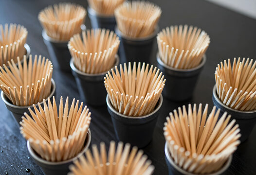 Numerous wooden toothpicks in small black metal cups arranged on a dark surface, hygiene and party supplies
