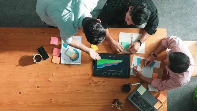 Top view of skilled project manager talking about financial graph to investors while sitting at meeting table with data analysis document. Diverse team discussing and brainstorming idea. Convocation.