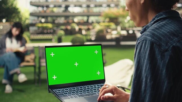 Isolated chroma key laptop mockup appears as a college student uses the trackpad outdoors on campus, with copy space for editable screen replacement, education content and digital learning visuals.