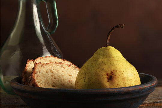 Pear and Bread Still Life. An Anjou Pear and slices of bread bread on a rustic wooden table with a mottled brown background.