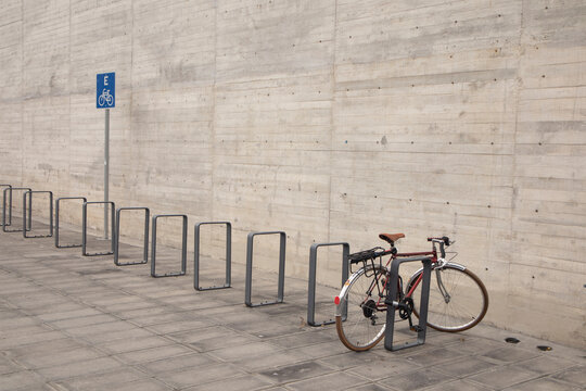 A bicycle parked at a designated bike rack area beside a large minimalist concrete wall