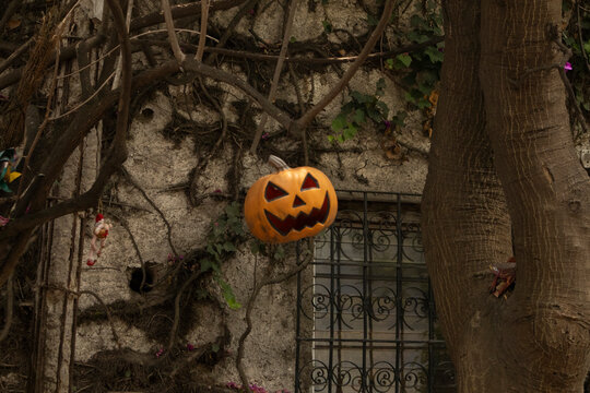 A carved jack-o'-lantern with a classic spooky face hangs in front of an aged stone wall
