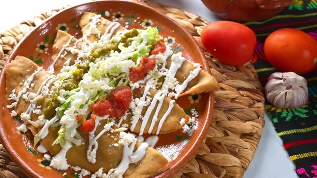 Mexican style chicken molotes with lettuce, sour cream, queso fresco, green salsa, and red sauce on a traditional clay plate