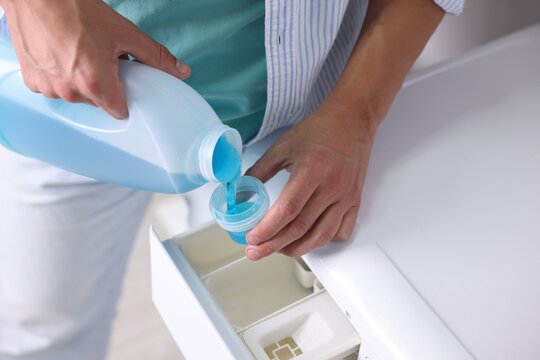 Man pouring liquid laundry detergent from bottle into cap near washing machine, closeup